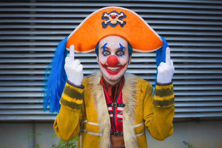 A clown in vibrant orange pirate costume and makeup smiling with colorful expressions.