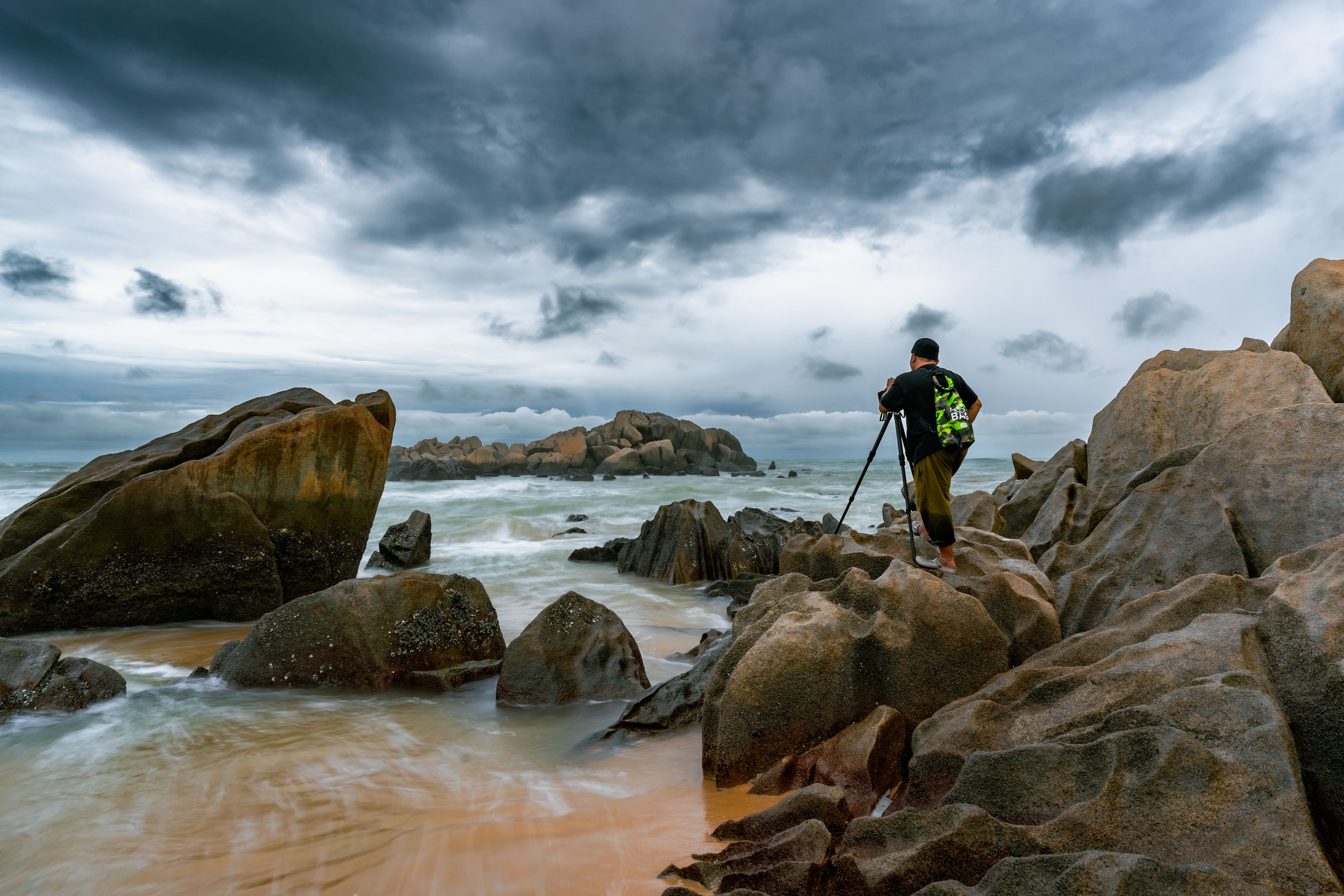 Photographer capturing stormy coastal landscape in Kijal, Malaysia, on a rocky shore.