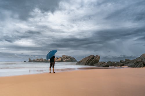 A Man with an Umbrella Standing on a Beach under a Cloudy Sky 