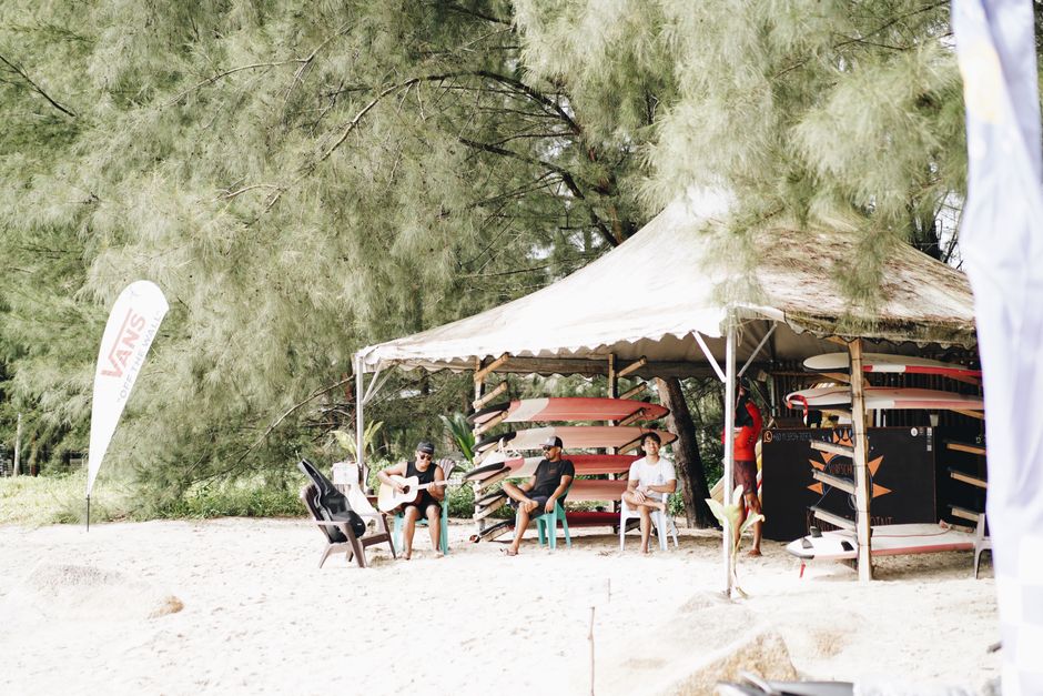 Group of friends enjoying leisure time at a beach tent with surfboards and guitar.