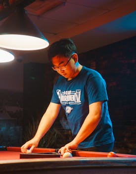 Young man focusing on billiards game in dimly lit bar setting.