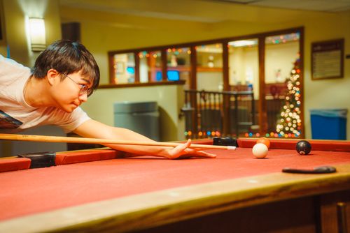 Free A young man skillfully plays pool in a cozy indoor setting with a Christmas tree in the background. Stock Photo