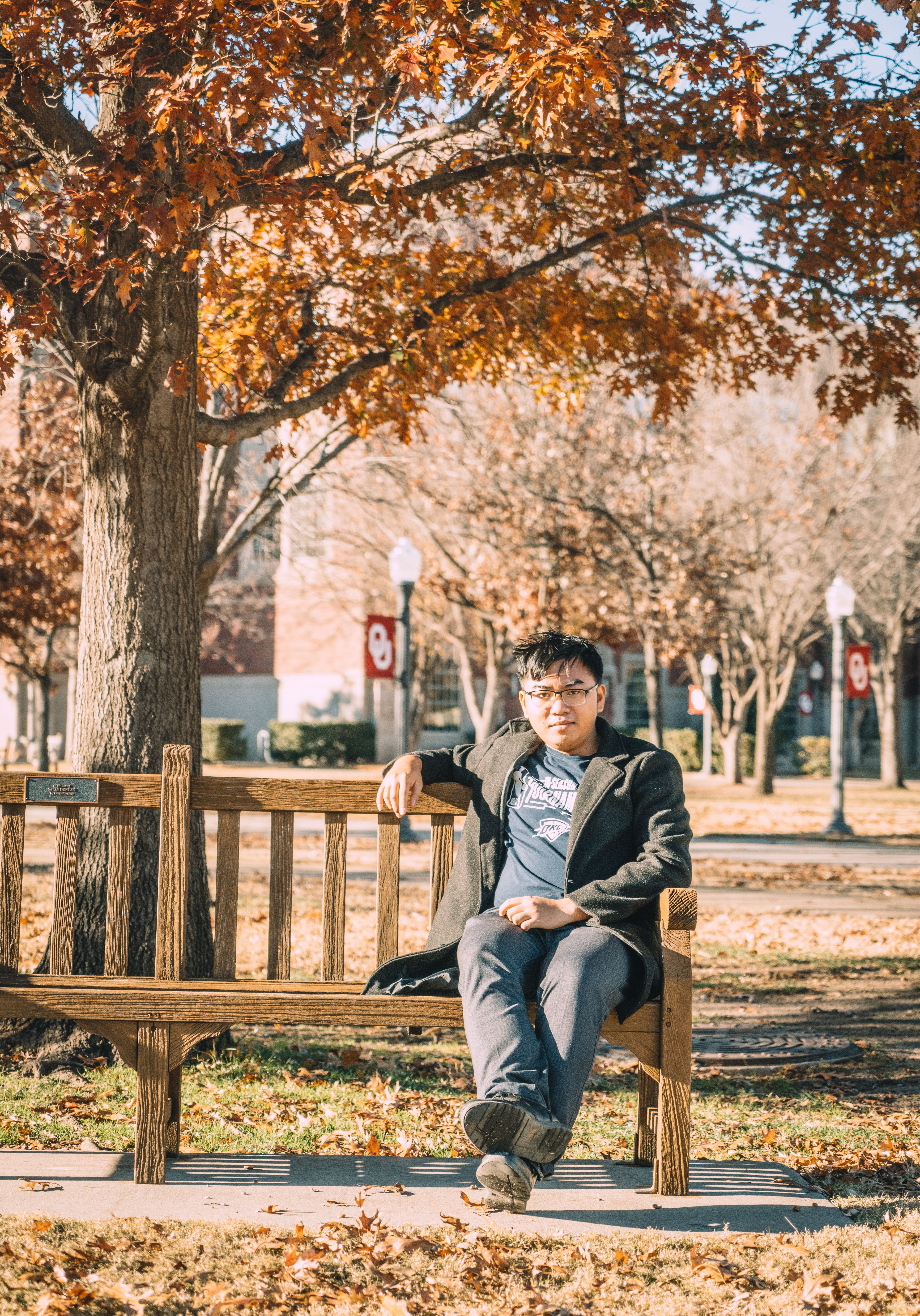 Man enjoying a sunny autumn day while sitting on a park bench surrounded by colorful leaves.