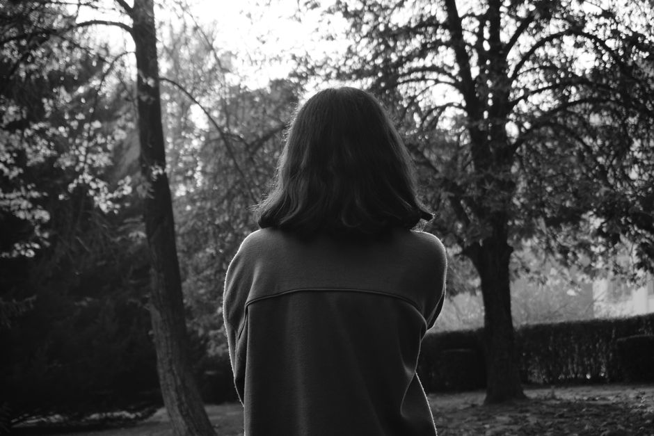 Black and white photo of a woman in a forest, backlit by soft sunlight.