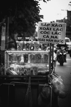 Black and white photo of a street food cart with a Vietnamese sign, capturing urban life.