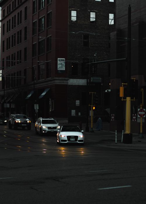 Free Evening view of cars driving on an urban street with city buildings in the background. Stock Photo