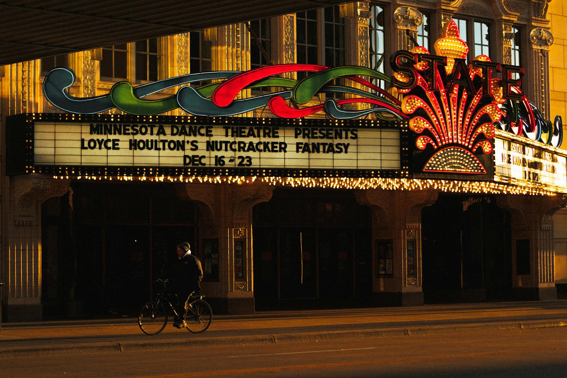 State Theatre in Minnesota illuminated at night showcasing a marquee and cyclist.