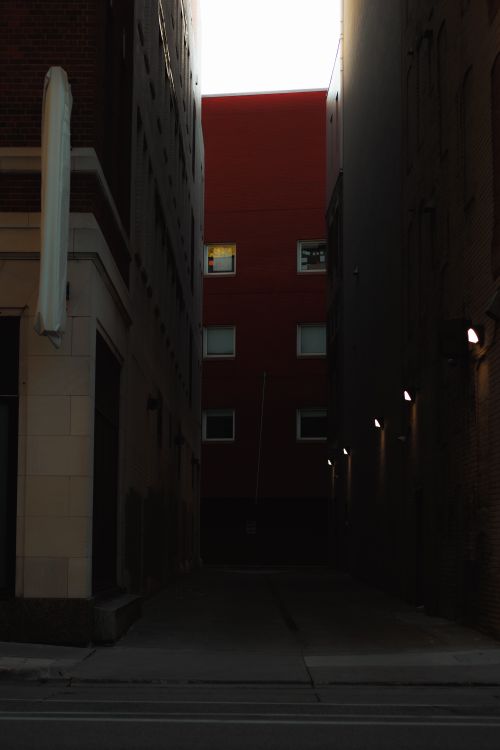 Free Moody urban alleyway with dim lighting and a bright red building lit by natural light. Stock Photo