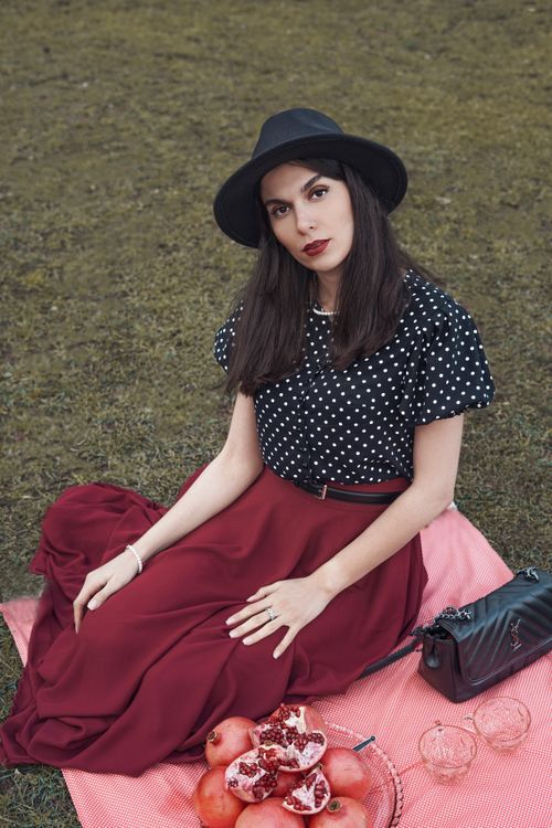 Free Stylish woman wearing a black hat and polka dot blouse sits elegantly on a picnic blanket. Stock Photo