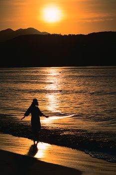 A serene silhouette of a woman enjoying the sunset by the sea shore, creating a peaceful vacation vibe.
