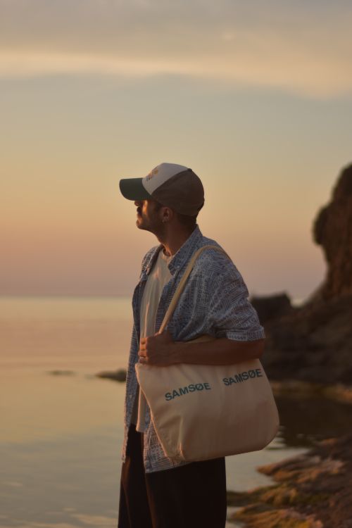 Free Man stands by the sea with a tote bag during sunset, enjoying the peaceful view. Stock Photo