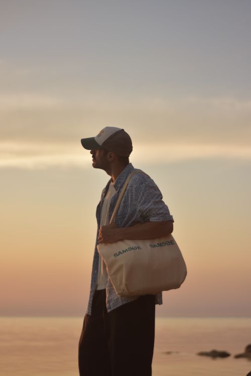 Free A man carrying a tote bag enjoys a serene beach sunset. Stock Photo