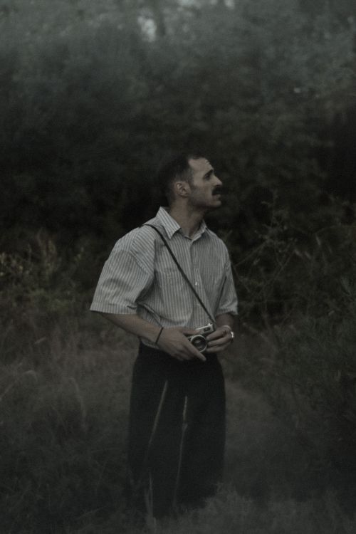 Free A man stands in a dark forest, observing with a vintage camera. Moody atmosphere. Stock Photo