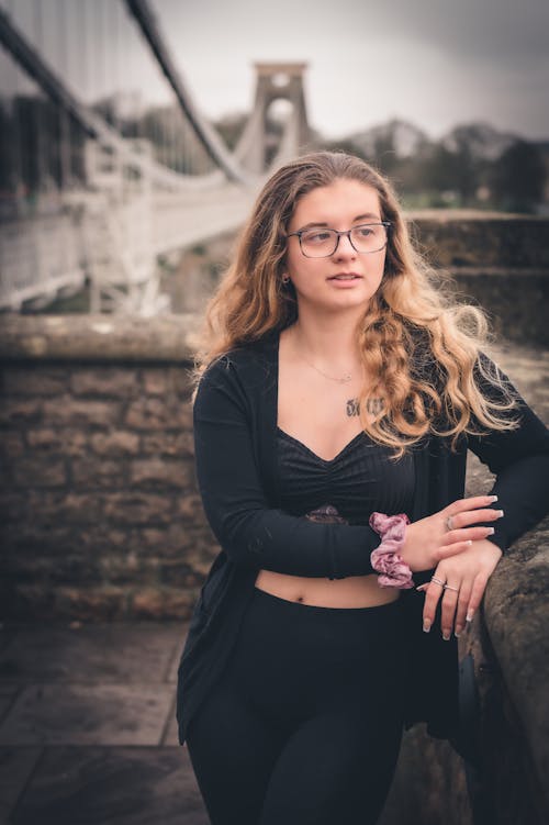 Woman in Eyeglasses Leaning on a Railing with a Bridge in the Background in Bristol, England