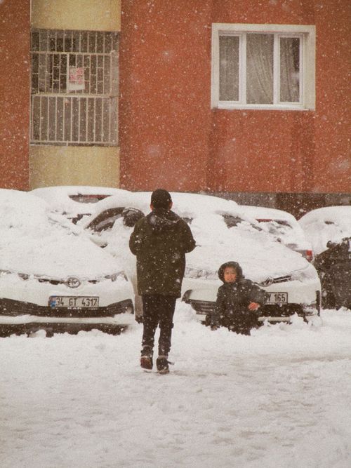 Free Two children playing in a snowy urban area with parked cars, enjoying winter weather. Stock Photo