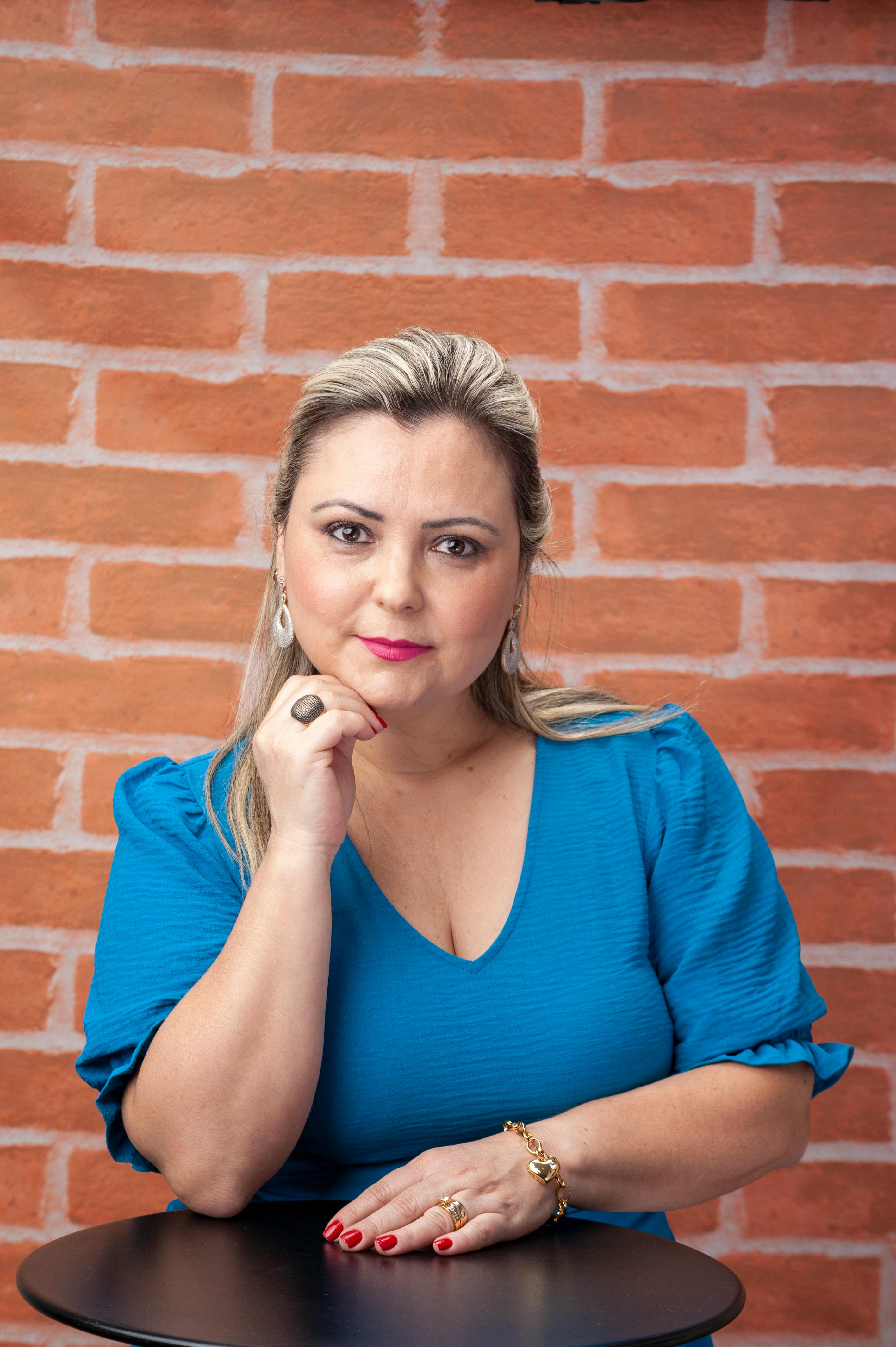 Stylish woman posing confidently in a blue blouse against a brick wall background.