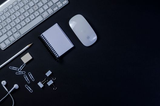 Flat lay of a modern workspace with keyboard, mouse, and stationery on a dark background.