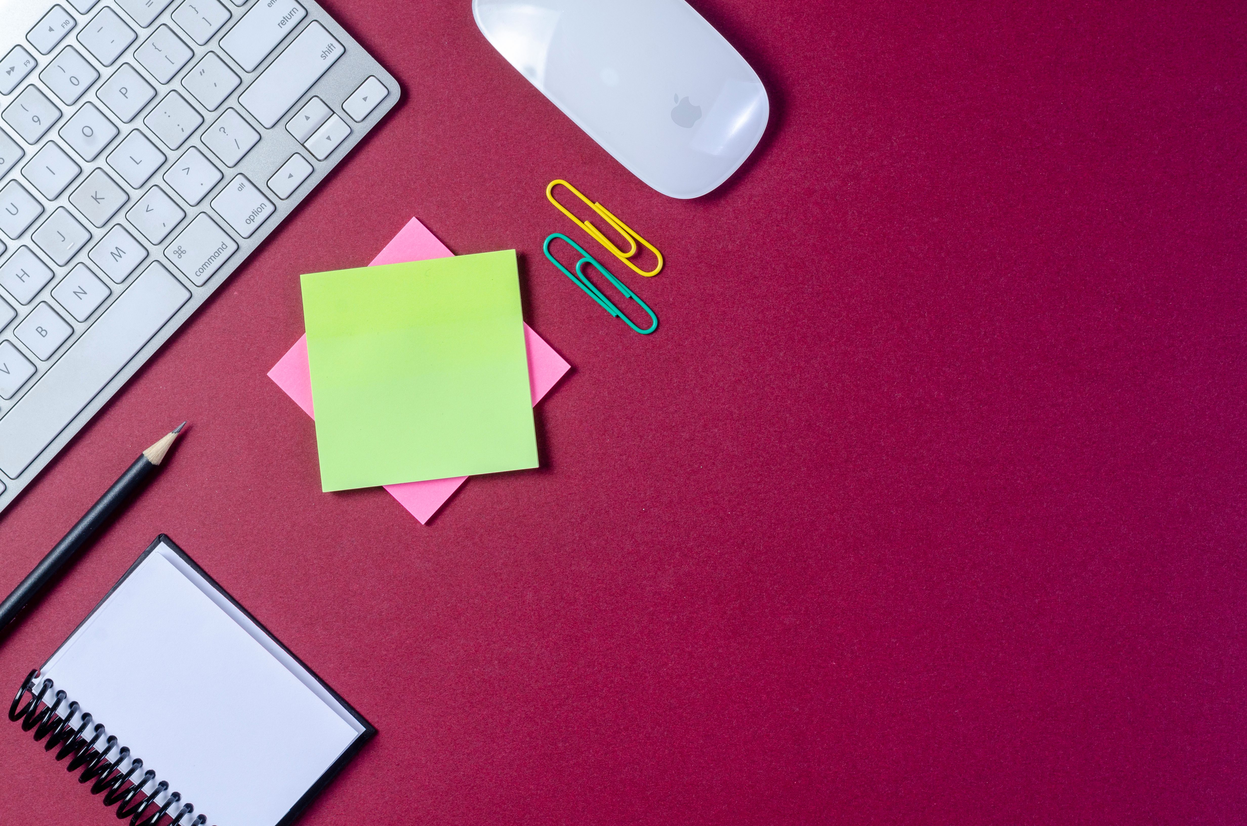 Flat lay of a vibrant office desk setup with keyboard, mouse, sticky notes, and stationery on a red background.