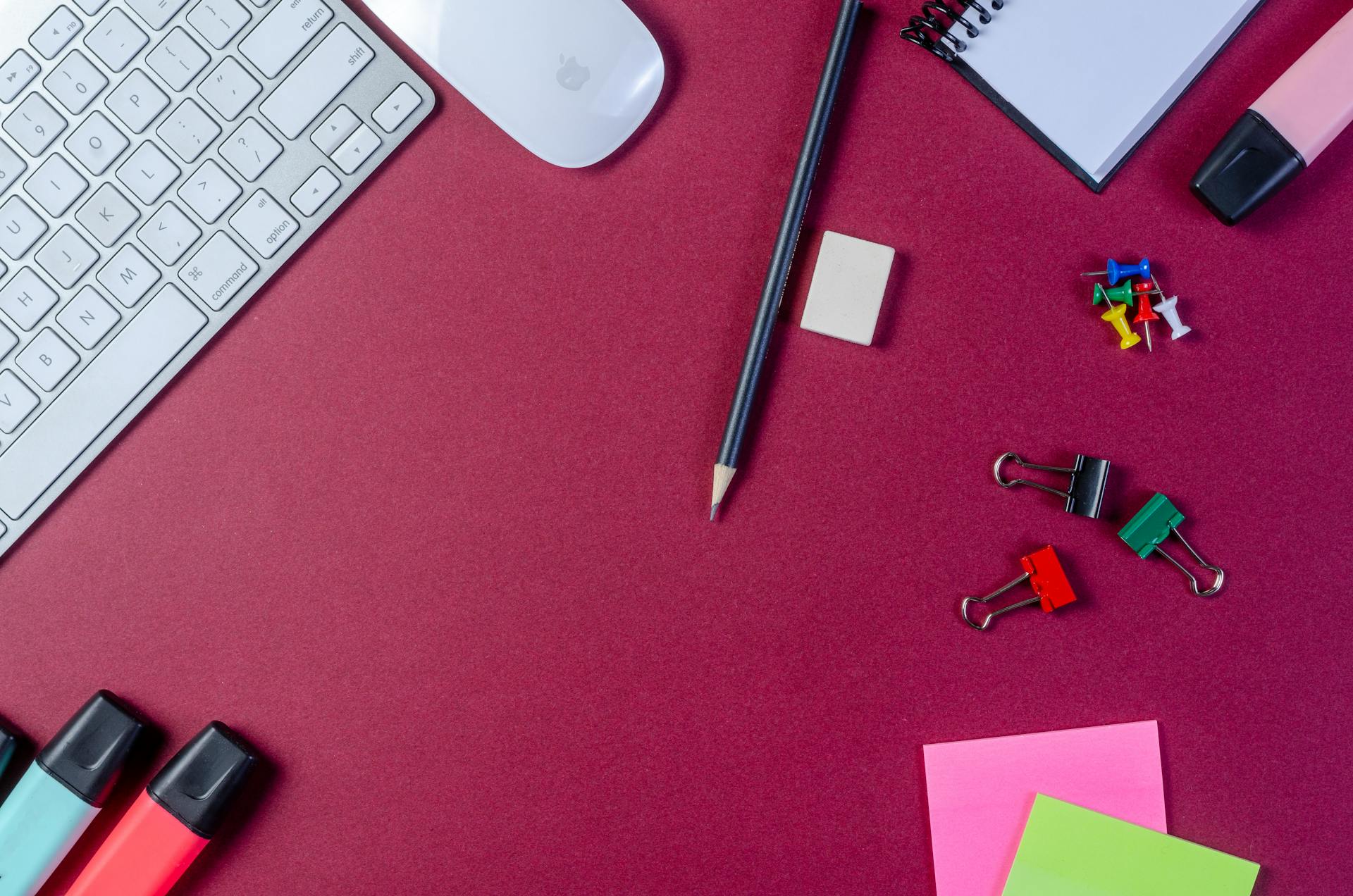 Flat lay of office supplies and keyboard on a red desk surface, perfect for business and education themes.