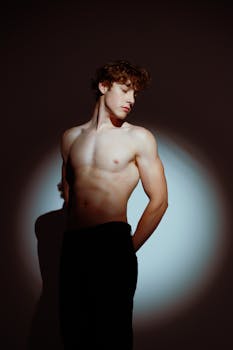 Artistic portrait of a shirtless young man posing in dramatic lighting.