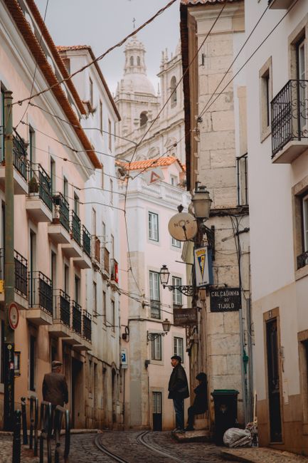 Explore a quaint Lisbon alley with tram rails and a view of the São Vicente de Fora monastery.