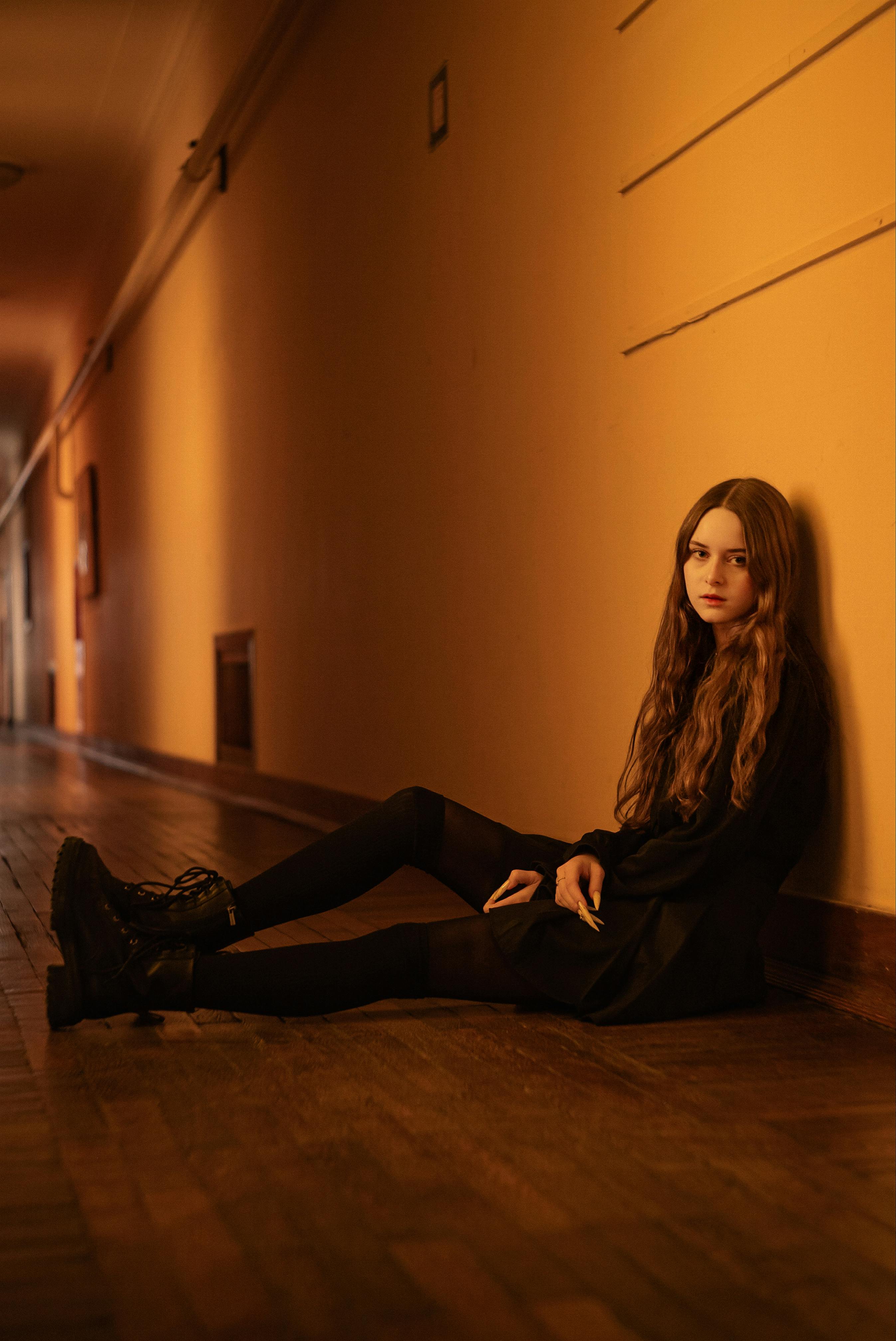 A young woman with long hair sits in a moody corridor, creating a thoughtful atmosphere.