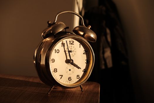 Old-fashioned alarm clock on wooden surface with warm lighting.