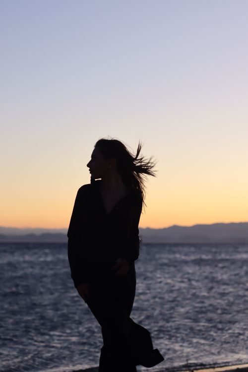 Free Silhouette of a woman against a vibrant sunset over the ocean, capturing a serene beach moment. Stock Photo