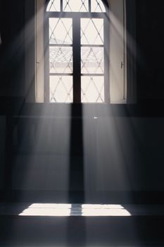 Sun rays beaming through a diamond-paned church window in Türkiye, creating a serene atmosphere.