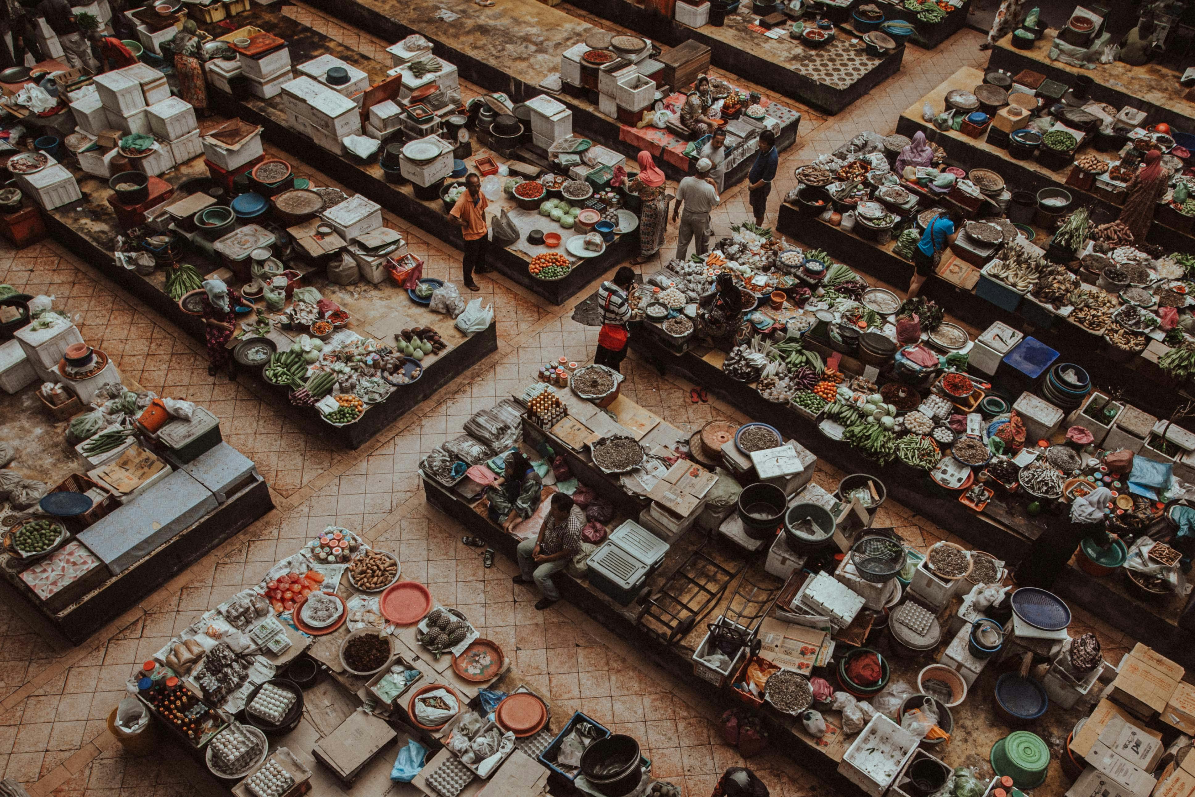 A bustling overhead view of an urban market with various stalls selling fresh produce and goods.