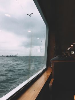 A serene view of the ocean and distant ships from inside a ferry with passengers.