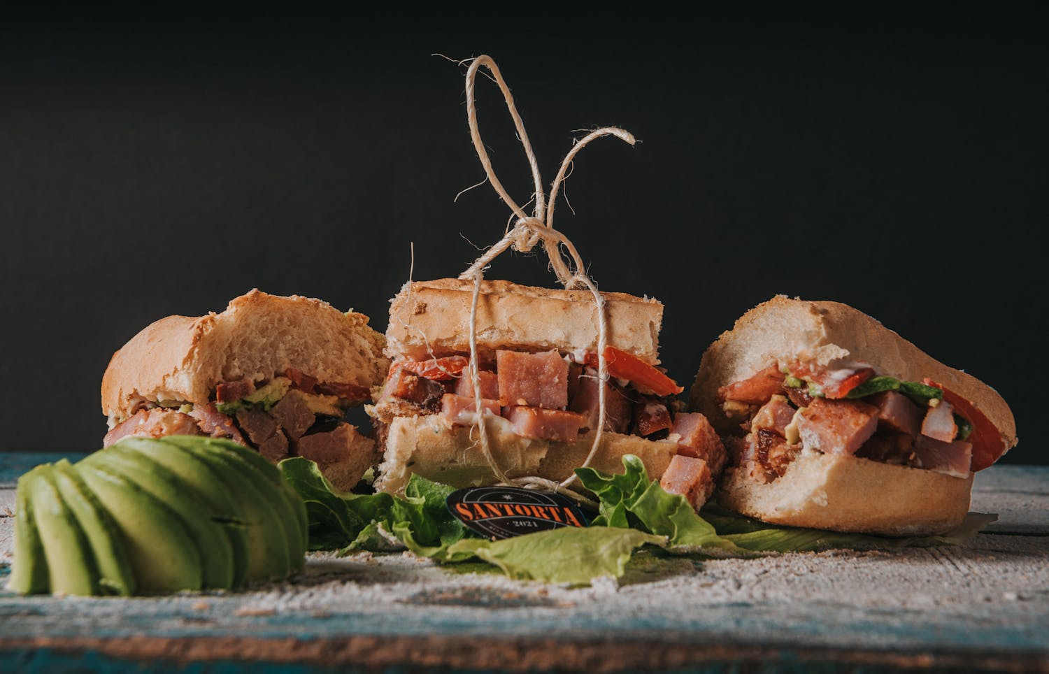 Close-up of a gourmet sandwich with fresh avocado slices and lettuce on rustic wood.