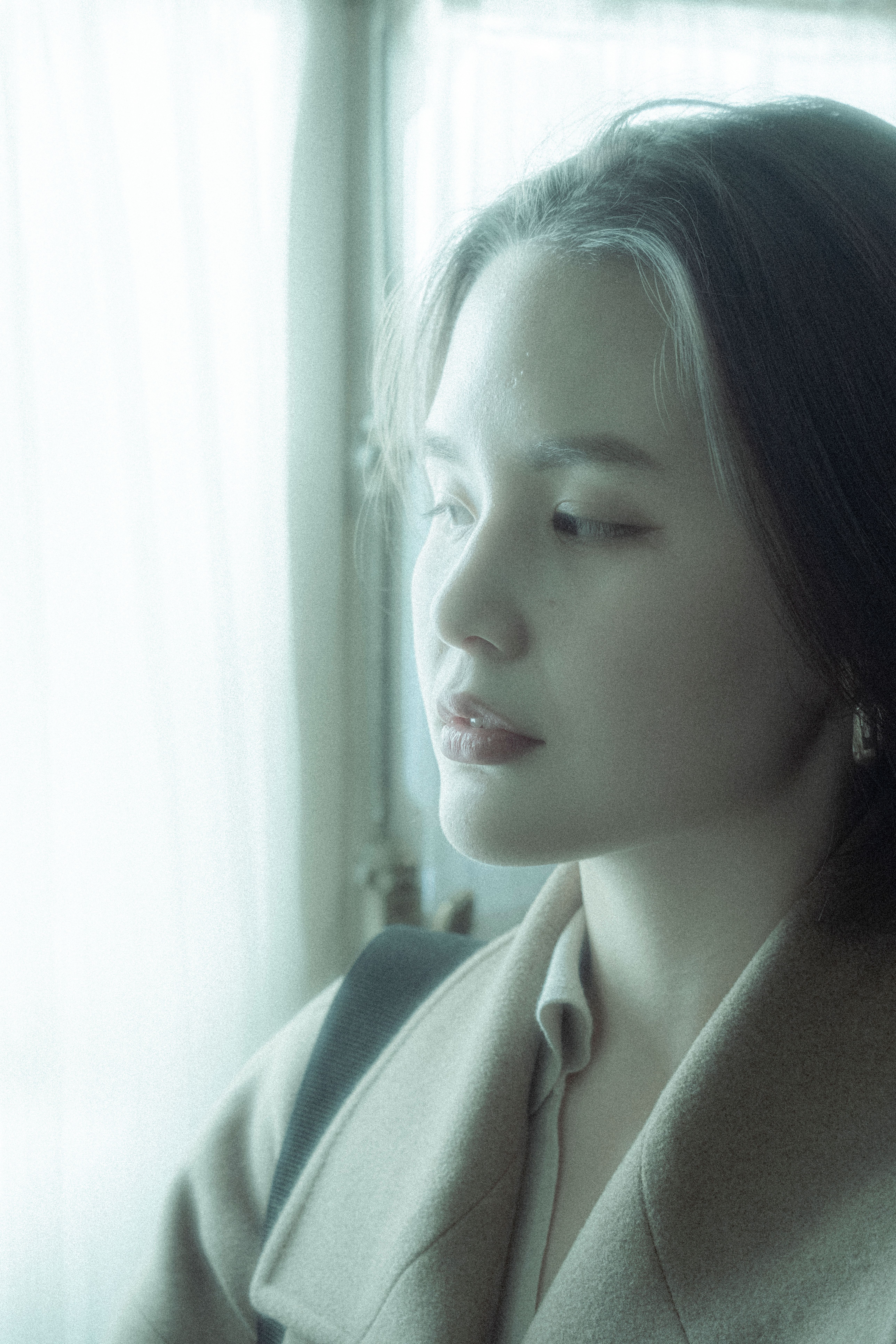 Soft focus portrait of an Asian woman gazing out a window, exuding calm and contemplation.