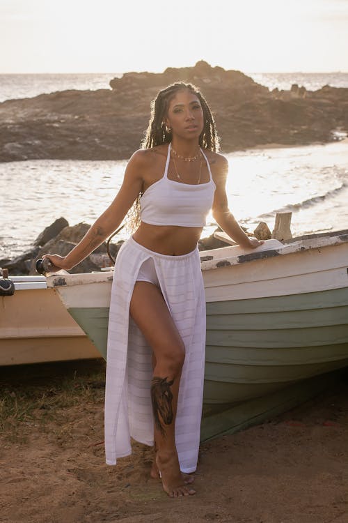 Young Woman in a White Tank Top Leaning against a Boat on the Beach