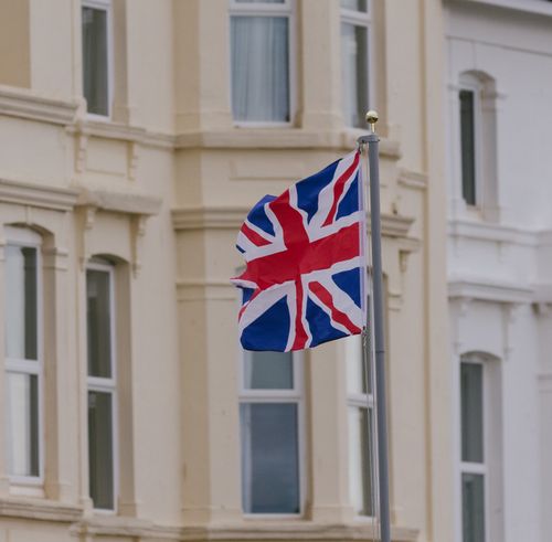 Free Union Jack flag waving proudly on a flagpole outside a classic building, symbolizing British pride. Stock Photo