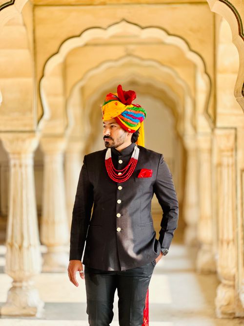 Free Elegant Indian man in traditional attire, standing in an ornate archway with colorful turban and decorations. Stock Photo