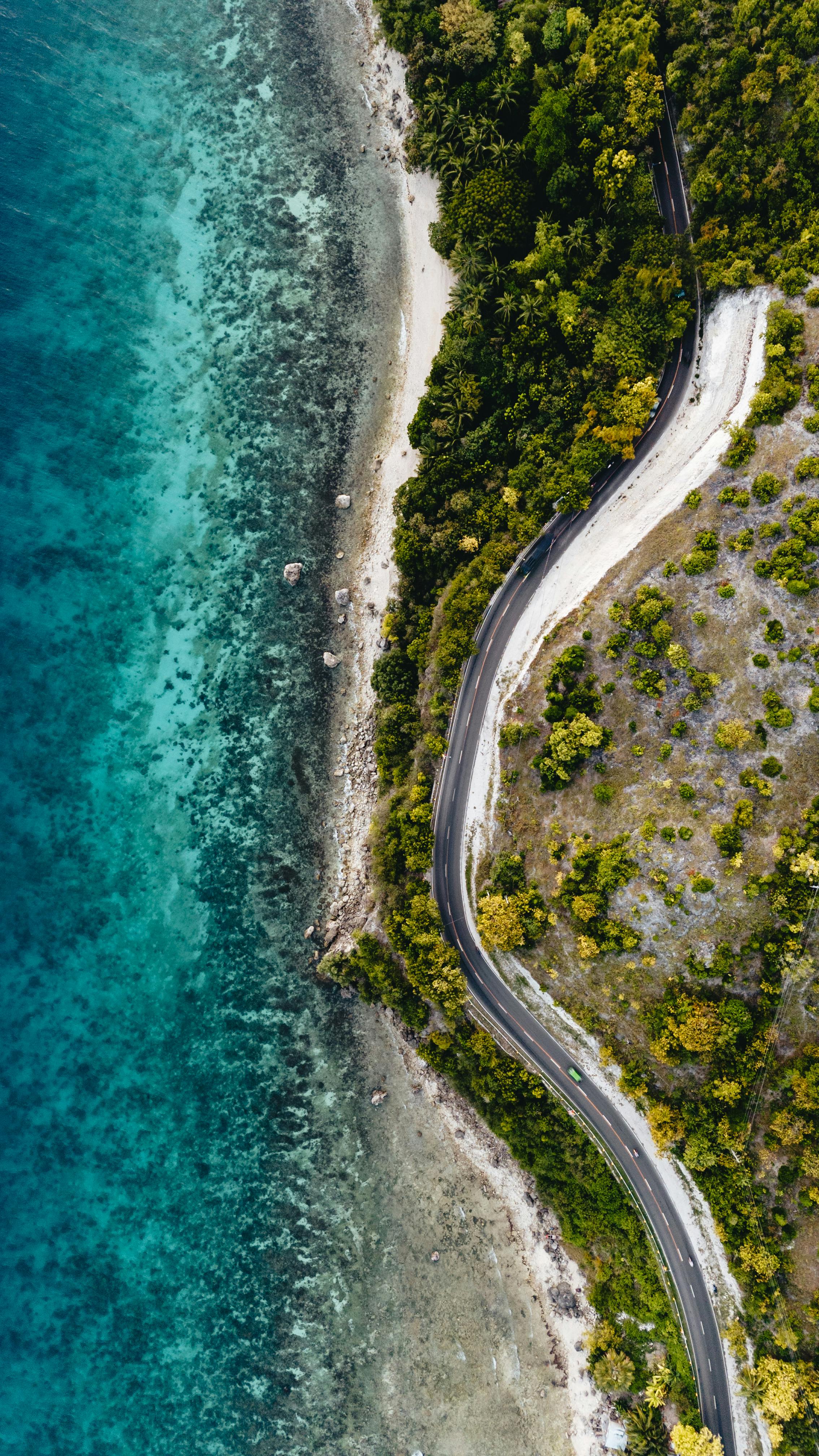 Stunning aerial shot of a winding coastal road in Central Visayas, Philippines with lush greenery and clear blue waters.