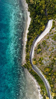 Stunning aerial shot of a winding coastal road in Central Visayas, Philippines with lush greenery and clear blue waters.