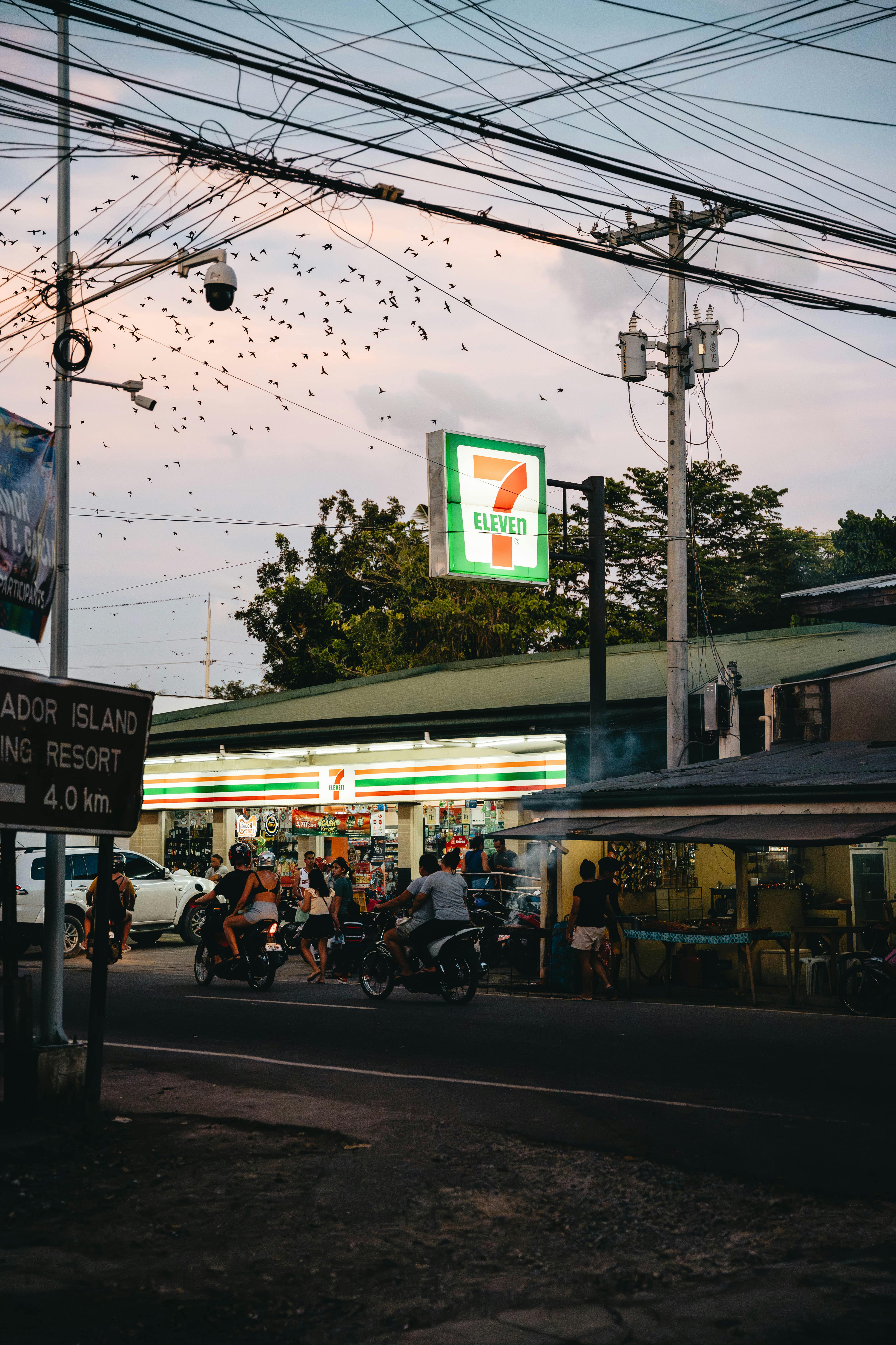 Vibrant street scene in Moalboal, Philippines, featuring a bustling 7-Eleven store at dusk.