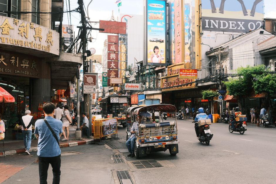 Scène animée de Chinatown à Bangkok avec des tuk-tuks et des enseignes vibrantes.