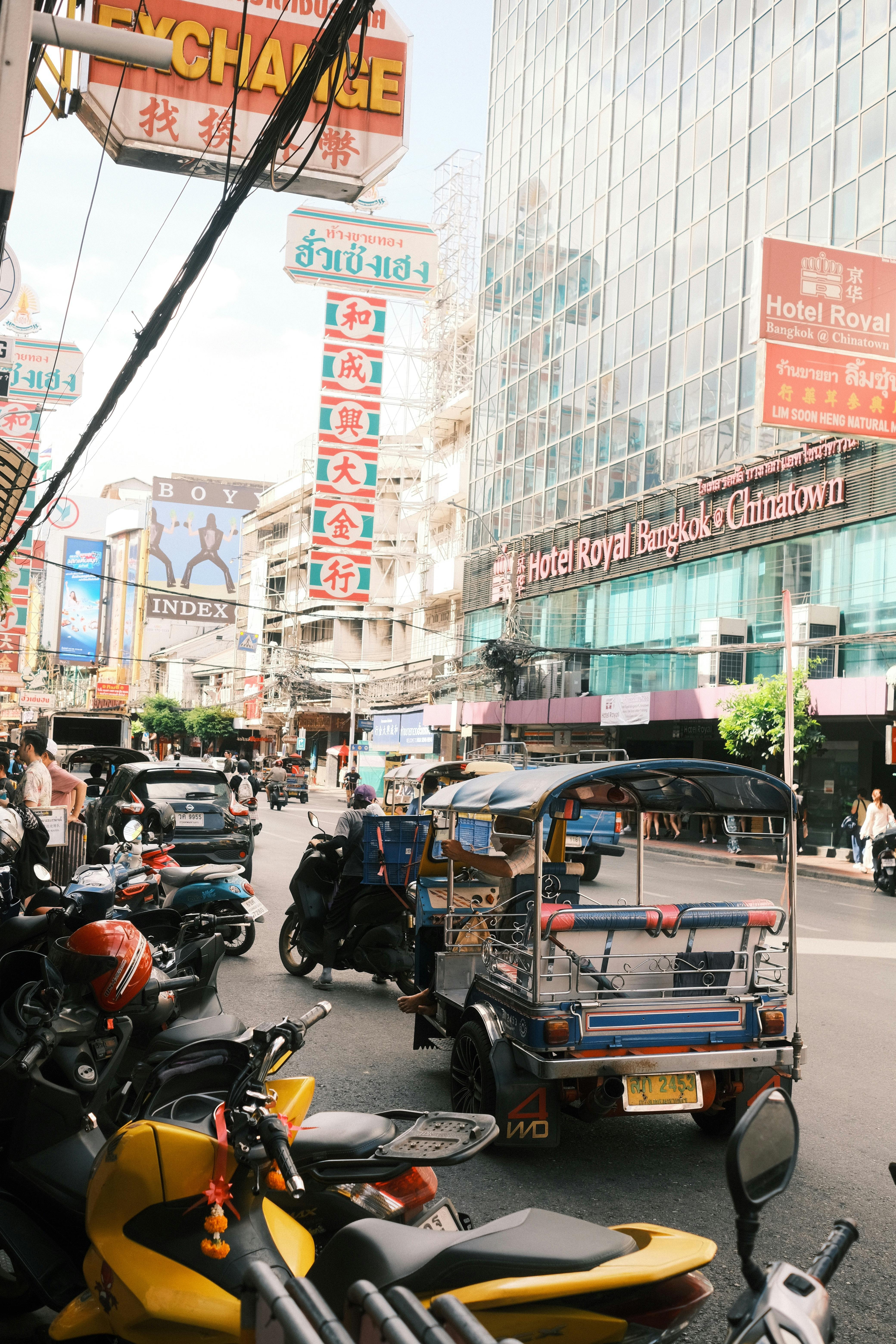 Vibrant street scene in Bangkok's Chinatown with tuk tuks, motorcycles, and colorful signs.