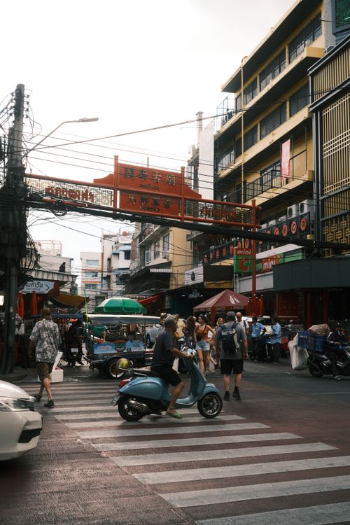 Free A lively street scene in Chinatown with pedestrians and scooters crossing under a red archway. Stock Photo