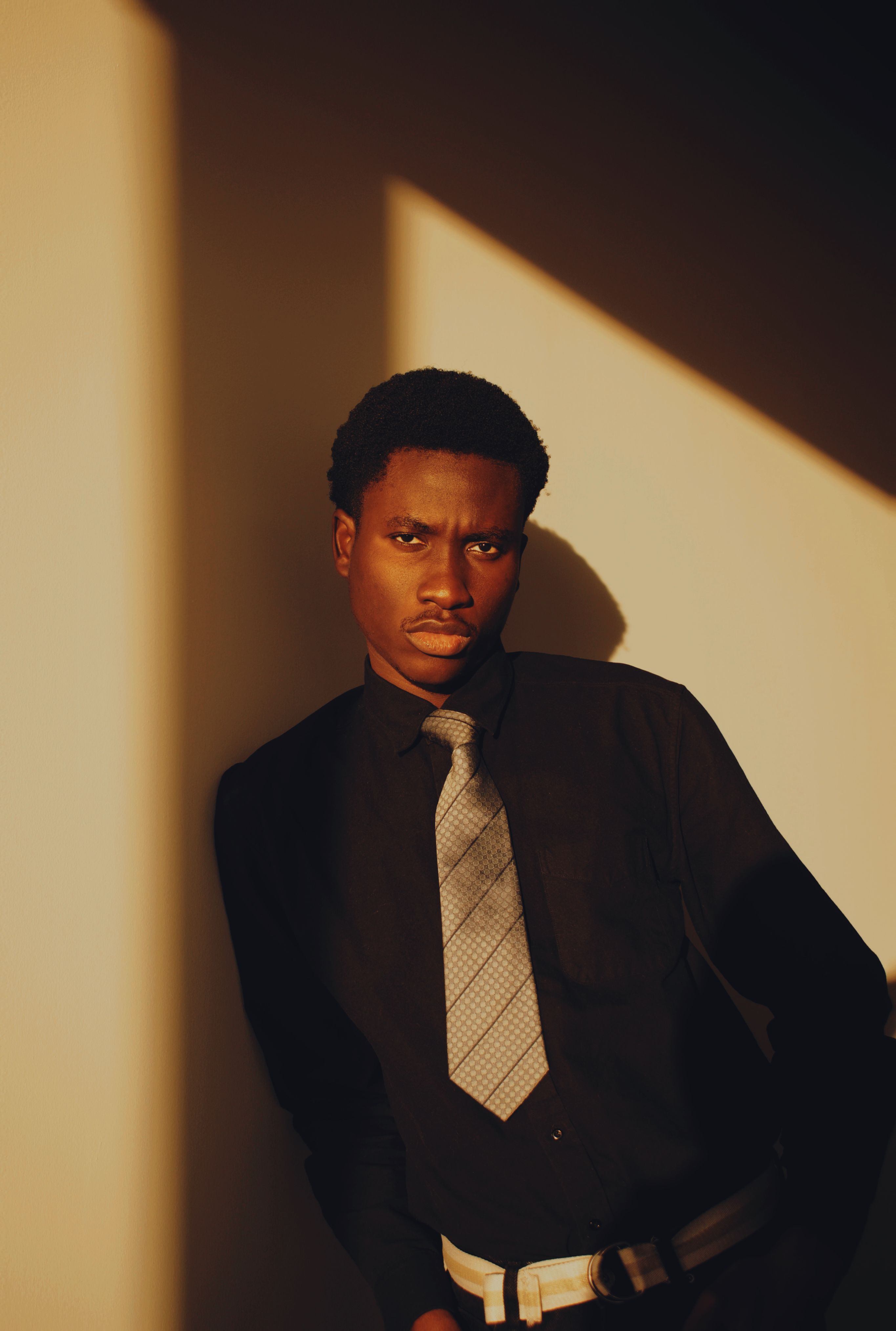 Elegant portrait of a man in a black shirt and tie against a shadowed backdrop.