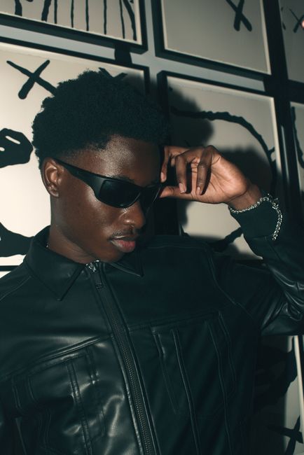 Fashionable man in leather and sunglasses posing against abstract wall.