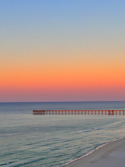 Free A stunning sunset over the ocean with a scenic view of a pier extending into the sea. Stock Photo