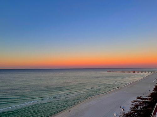 Free A vibrant beach sunset over calm ocean waves, with a distant pier in view. Stock Photo