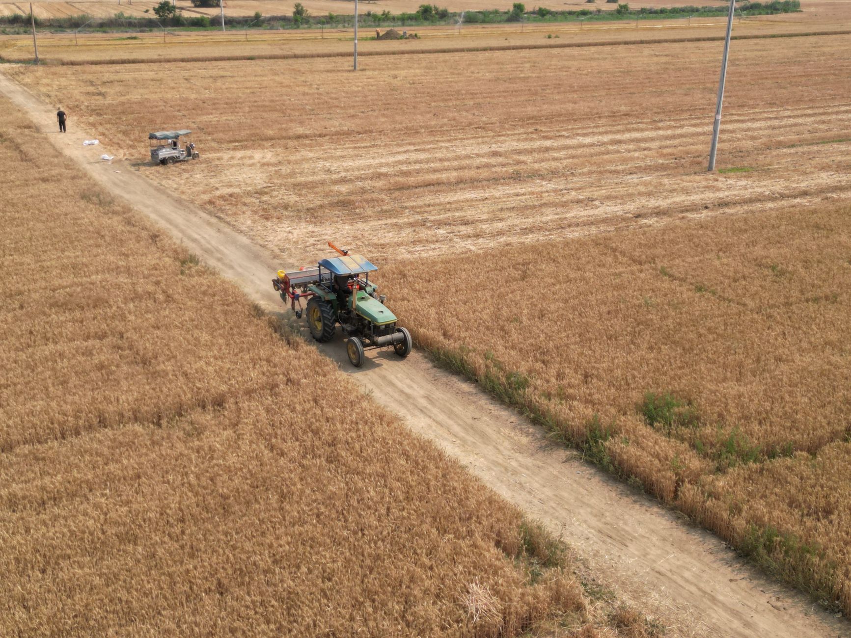 Drone shot of a tractor in a rural wheat field in Baoding, China, under clear skies.
