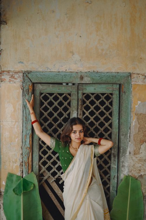 Free A stunning woman in traditional Indian attire posing against an antique window frame, exuding elegance and grace. Stock Photo