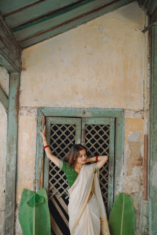 Free A woman elegantly poses in a traditional sari against a rustic textured wall, showcasing cultural beauty and grace. Stock Photo