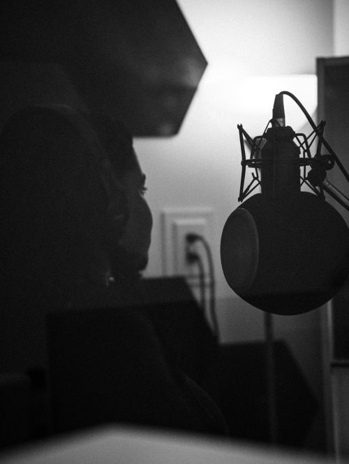 Free A black and white portrait of a musician recording in a studio, featuring a condenser microphone. Stock Photo